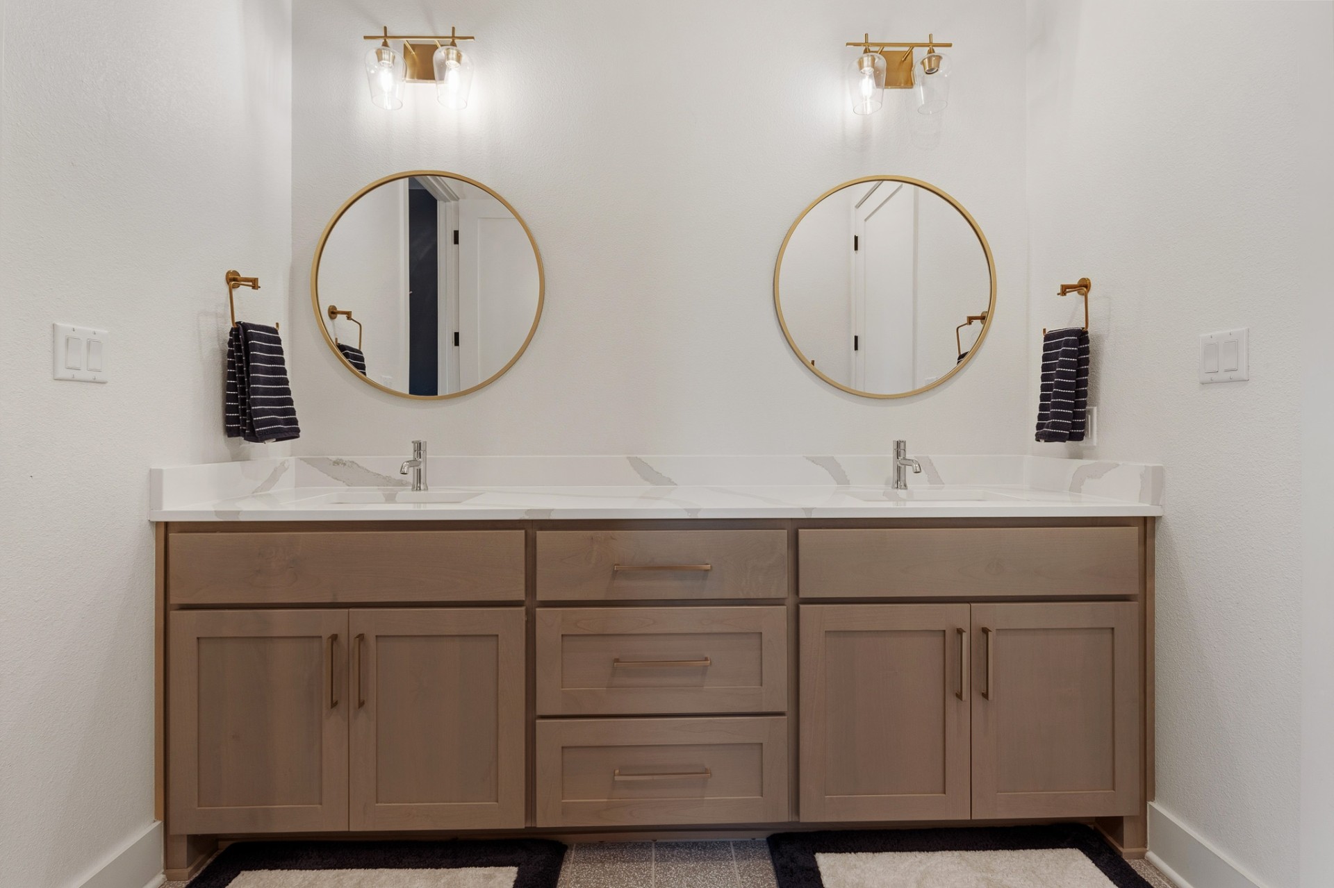 Jack-and-jill bath dual vanity front — tan shaker cabinets, round gold mirrors and gold sconce lights
