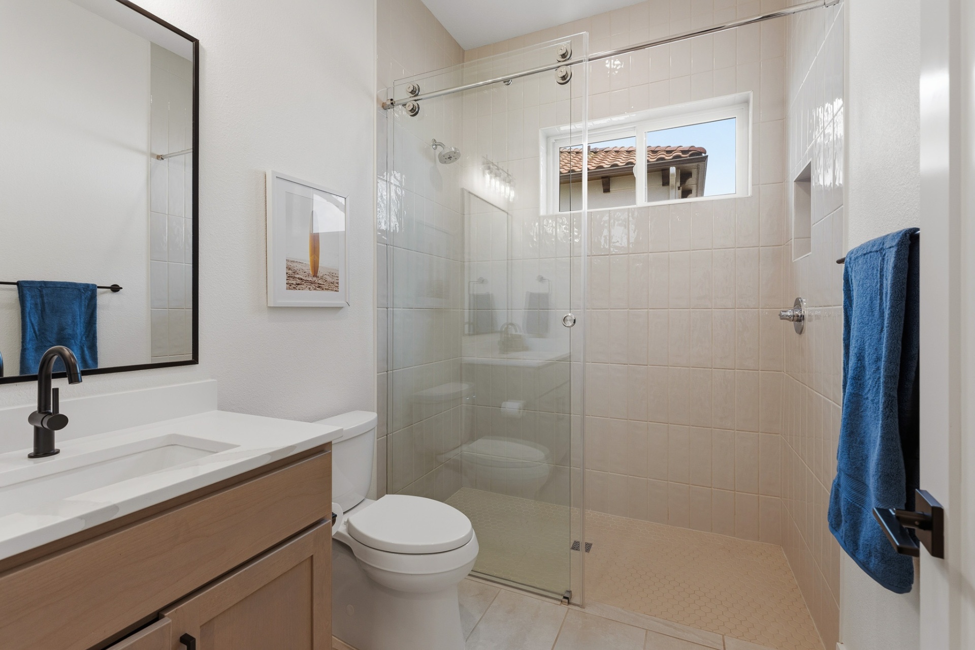 En-suite bath with glass sliding shower, tan tile, surfboard art and black fixtures