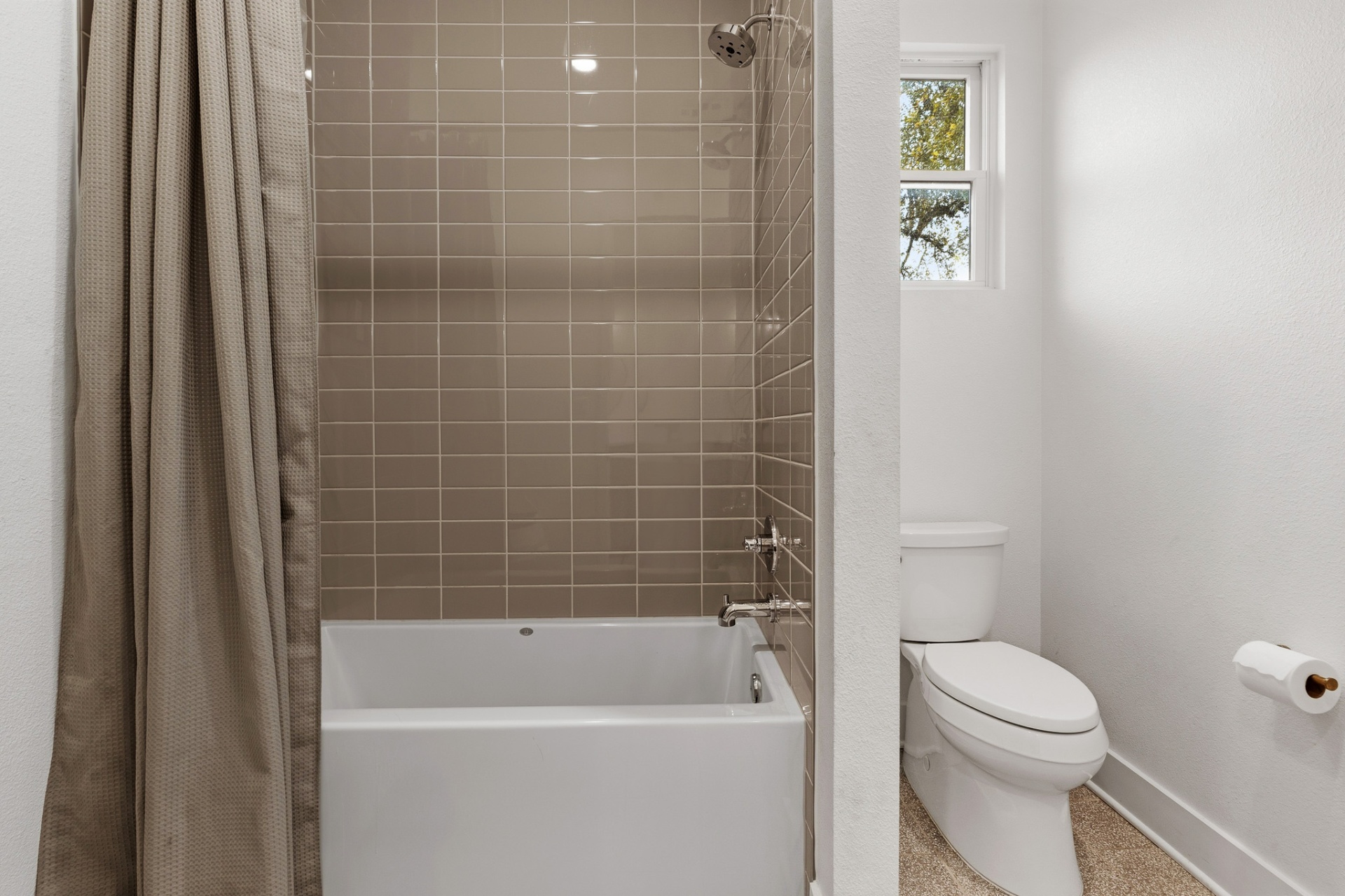 Shared bath tub/shower with taupe subway tile, curtain, window with oak tree view and toilet