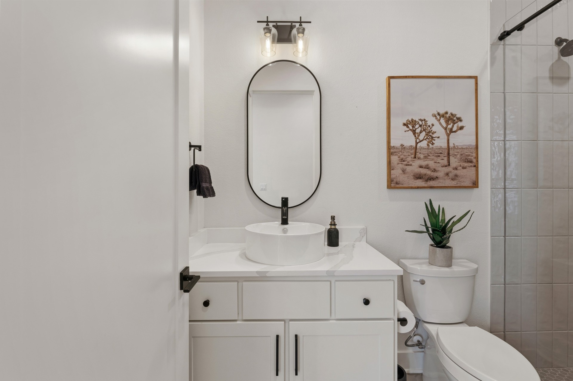 Guest bathroom with vessel sink, oval black-frame mirror, quartz countertop and walk-in shower