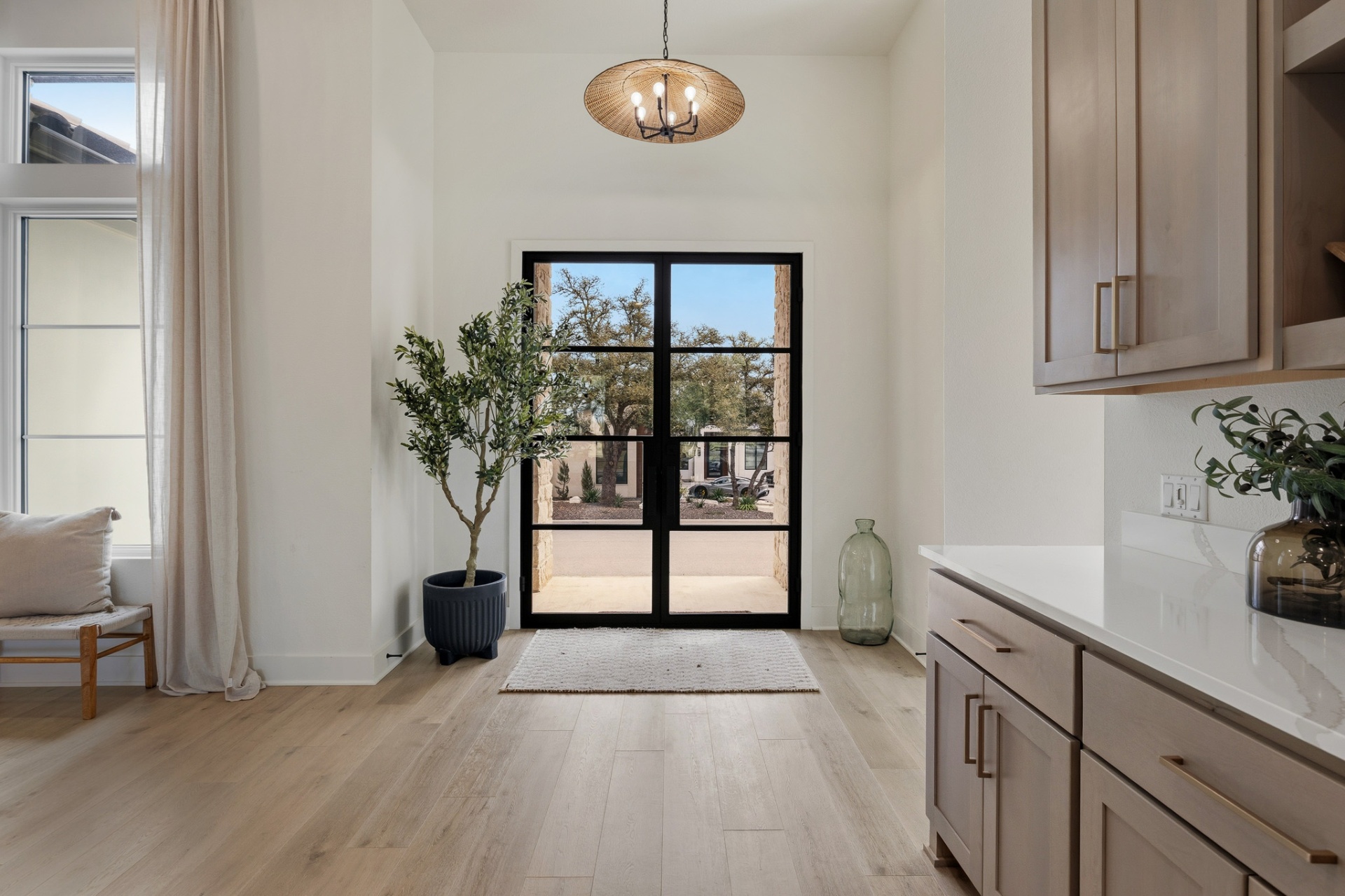 Front entry — black steel French door, olive tree, rattan chandelier and wet bar cabinets