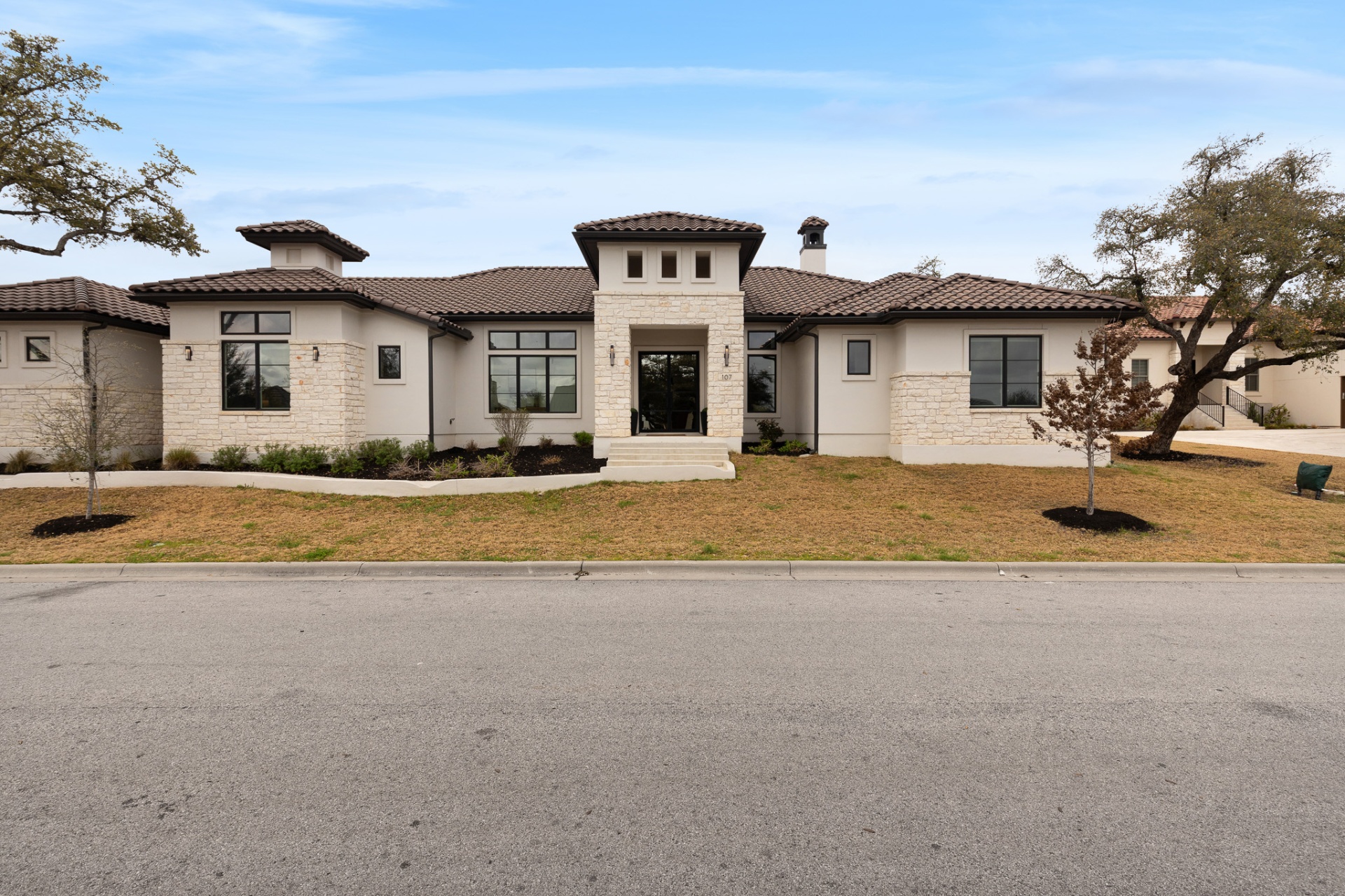 Front exterior centered — white stone, dark tile roof, double entry doors and curved driveway