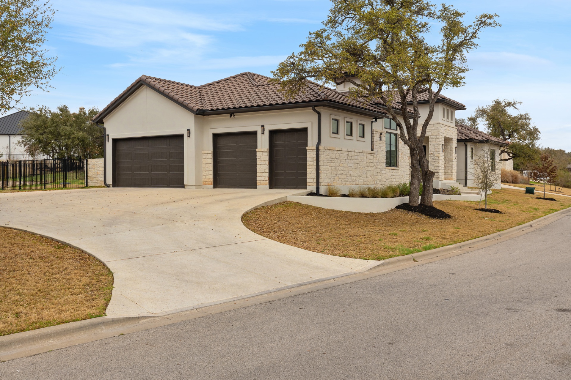 Front exterior left side — three-car garage with dark doors, curved driveway and white stone