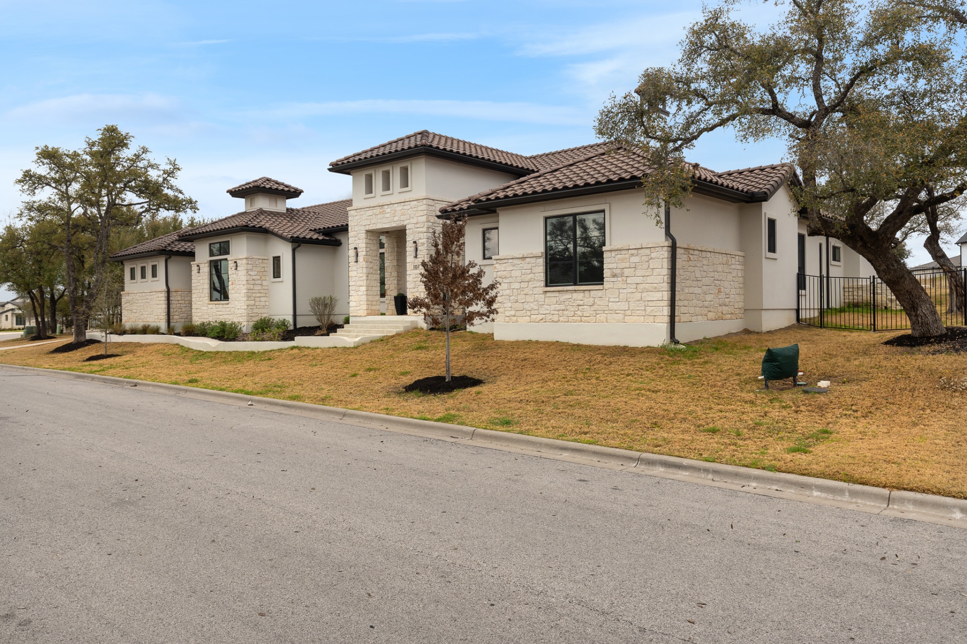 Front exterior from right — white stone, arched windows, grand oak tree and landscaped beds