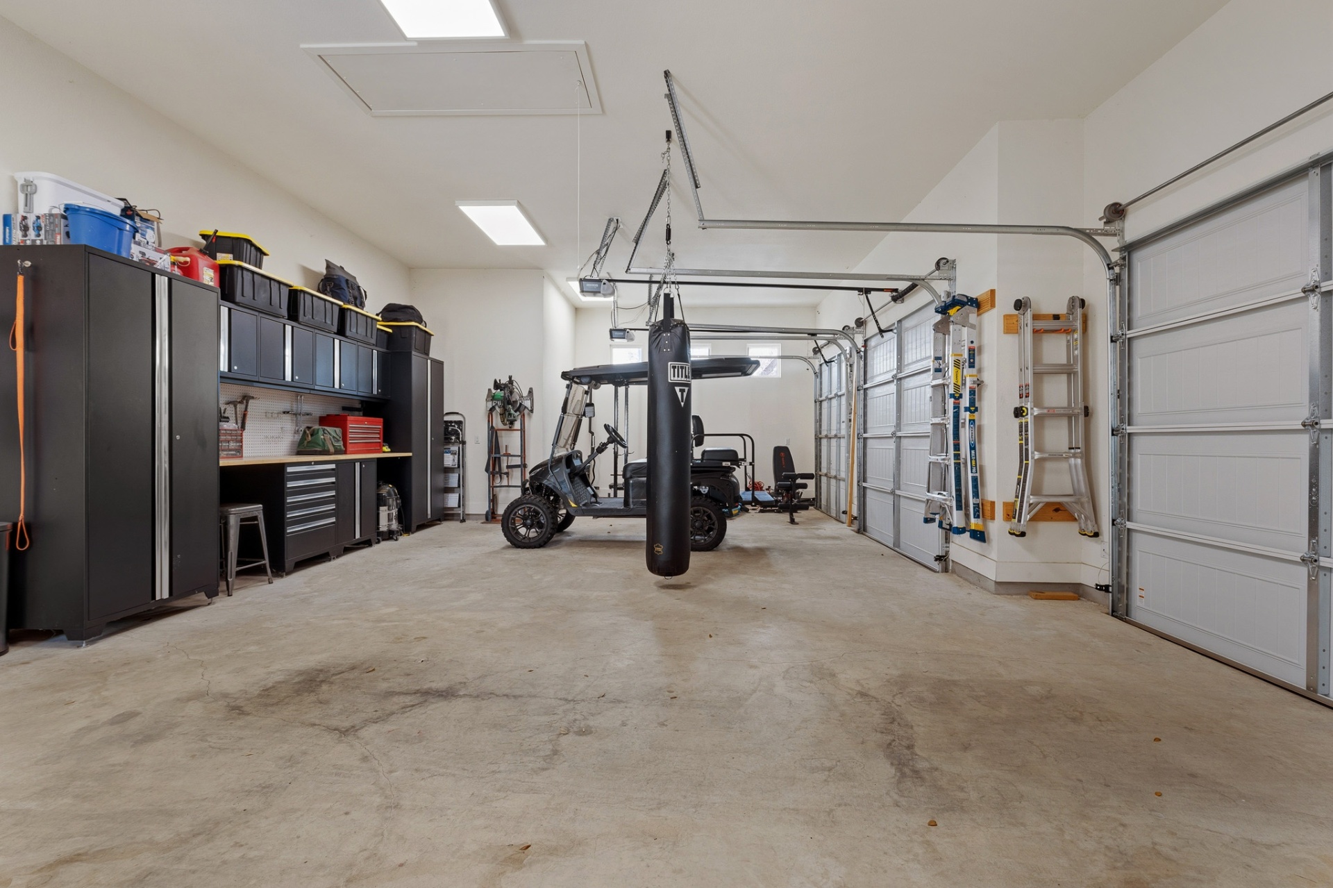 Garage workshop side — workbench, tool cabinets, punching bag, scooter and dual bay doors