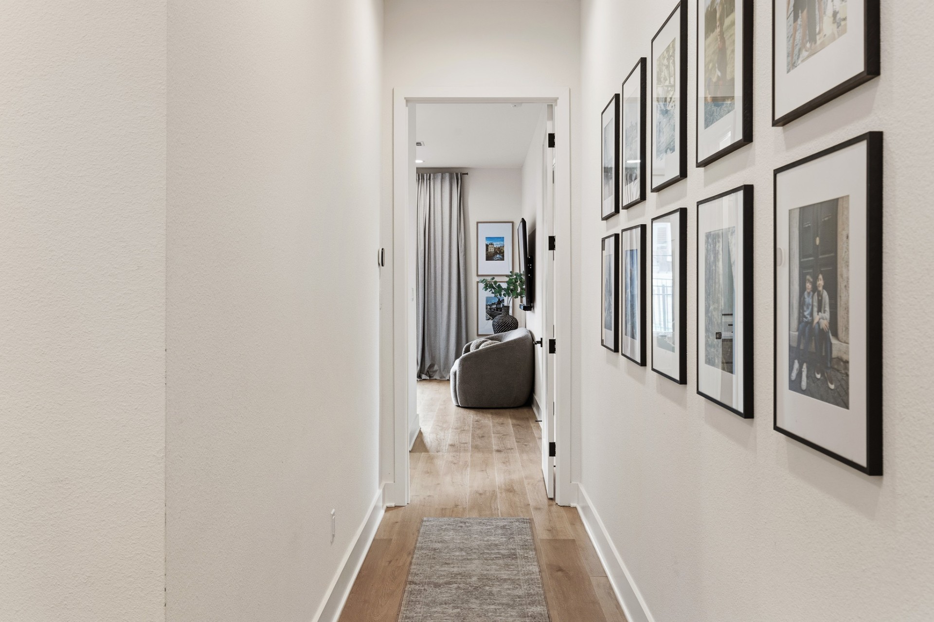 Hallway with wood-look floors, gallery wall of family photos and view to primary bedroom