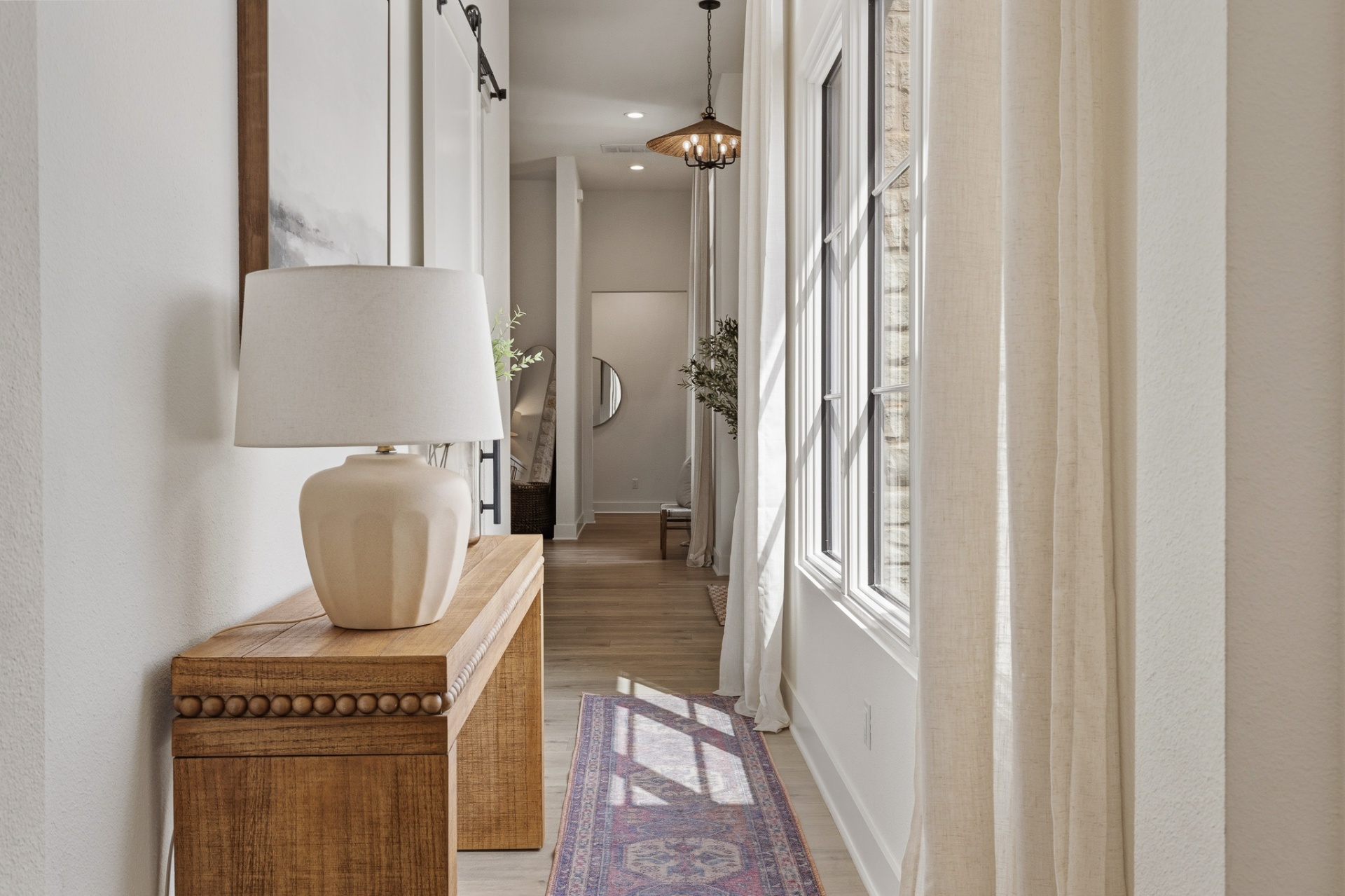 Primary wing hallway — wood console, ceramic lamp, runner rug and rattan pendant with barn door