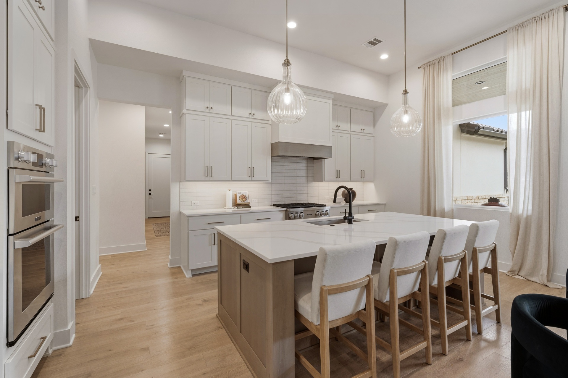 Kitchen island with bar seating, glass pendant lights, double wall ovens and subway tile backsplash