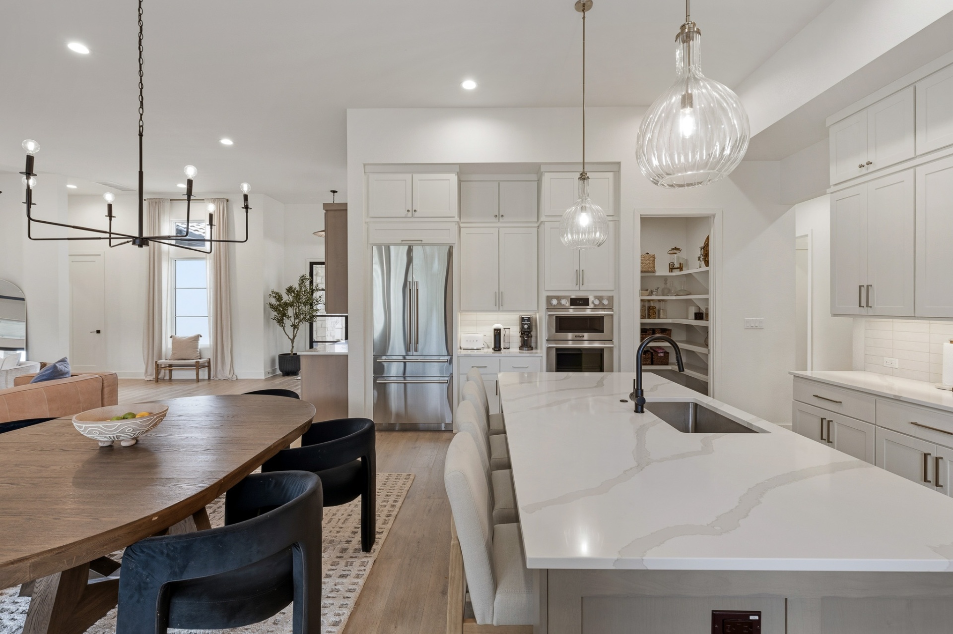 Chef's kitchen wide view — quartz island with seating, stainless refrigerator, double wall ovens and view to dining and living areas