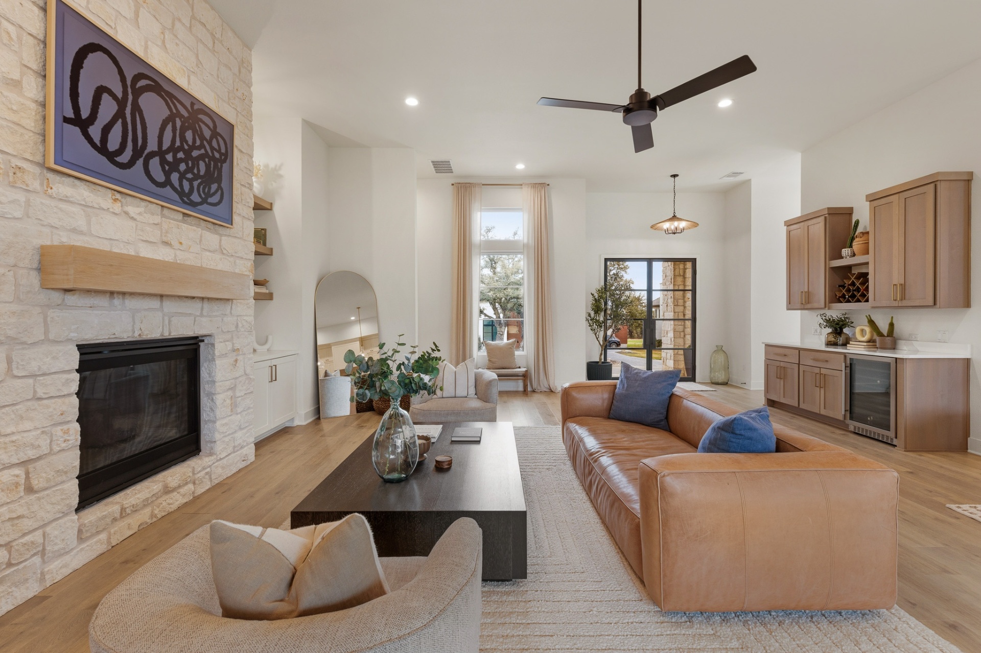 Living room with stone fireplace, wet bar nook, leather sofa, blue accent pillows and ceiling fan