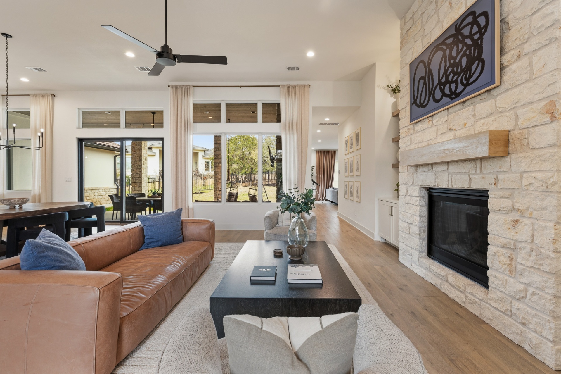 Living room — leather sofa, stone fireplace with art, patio doors with backyard view and dining area