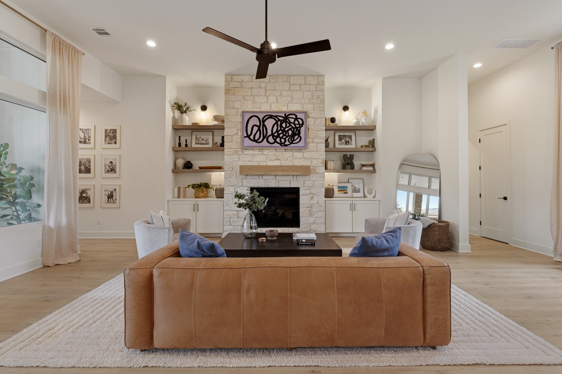 Living room — symmetrical stone fireplace wall with built-in shelving, leather sofa and ceiling fan