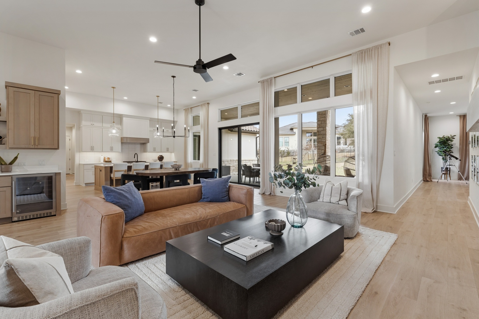Living room with floor-to-ceiling patio doors, leather sofa, kitchen island view and backyard natural light