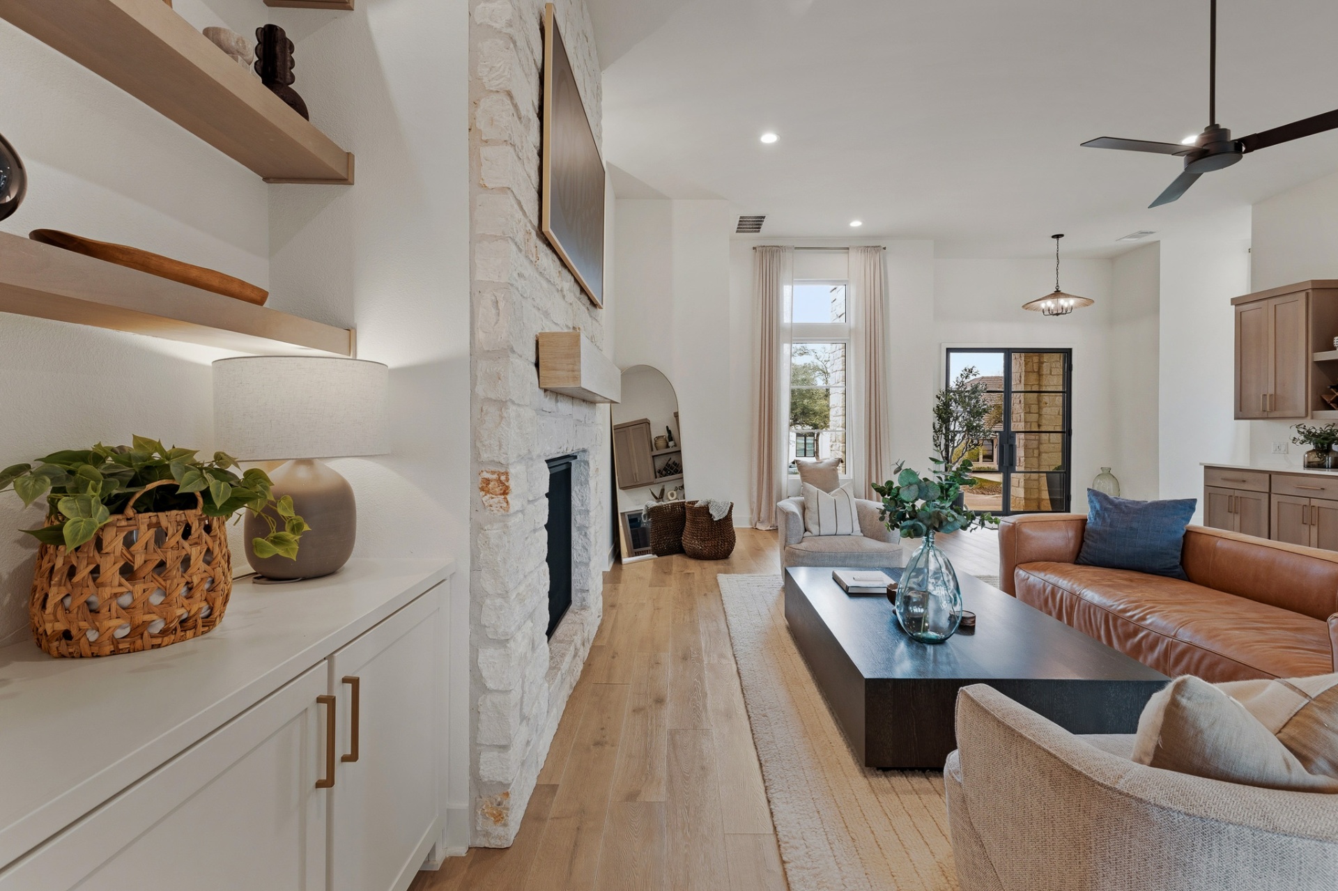 Living room fireplace close-up — floating shelves, stone surround, leather sofa and view to entry