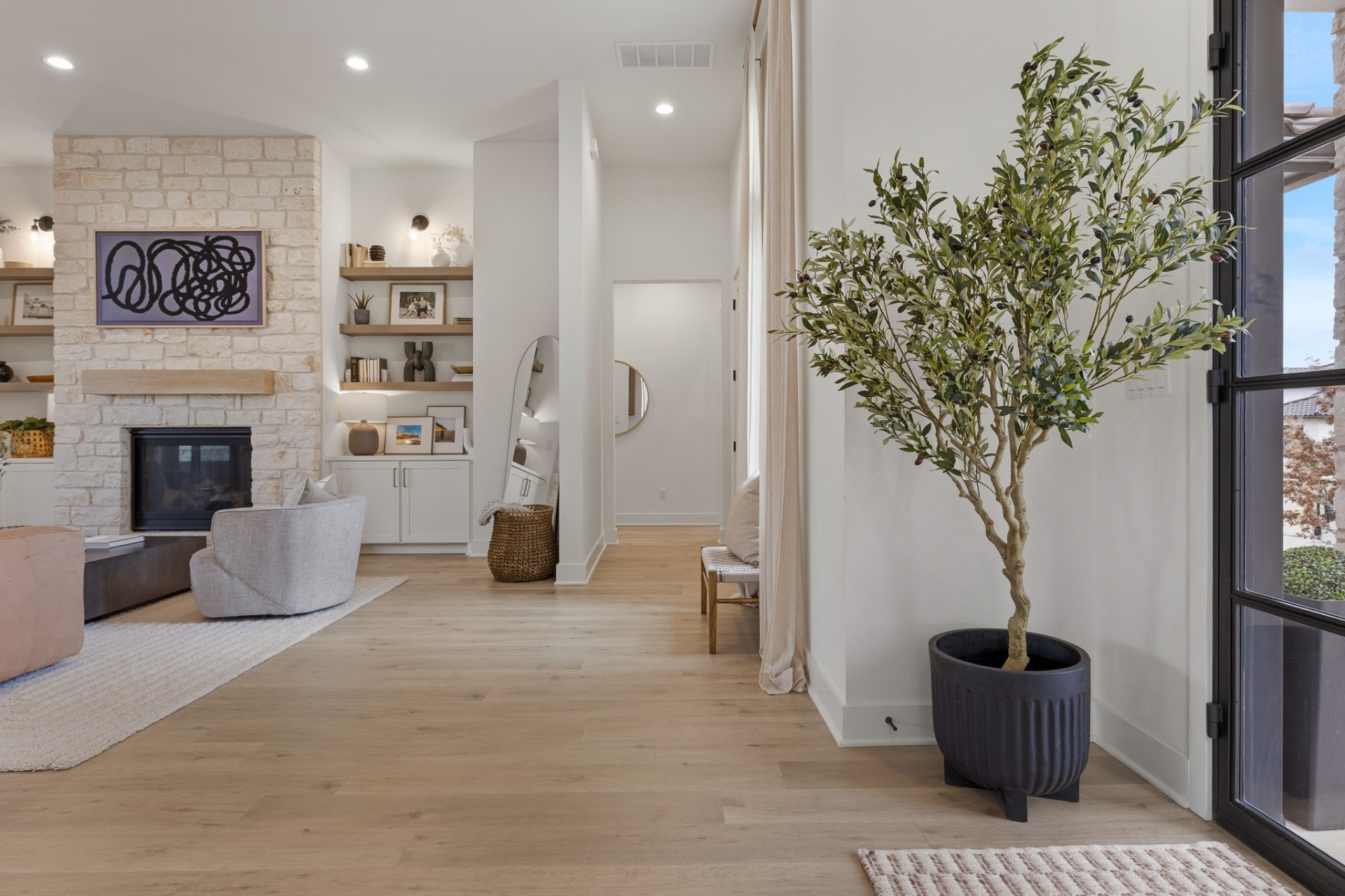 Entry foyer — olive tree, stone fireplace, built-in shelving, arched mirror and black steel front door