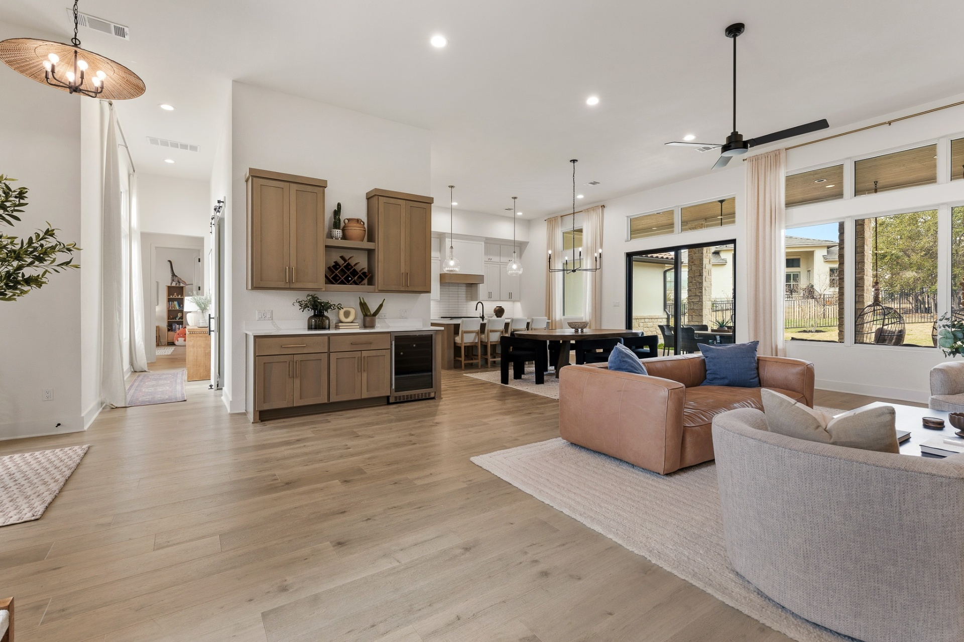 Open-concept living from wet bar — leather sofa, dining area, patio doors and kitchen pendants