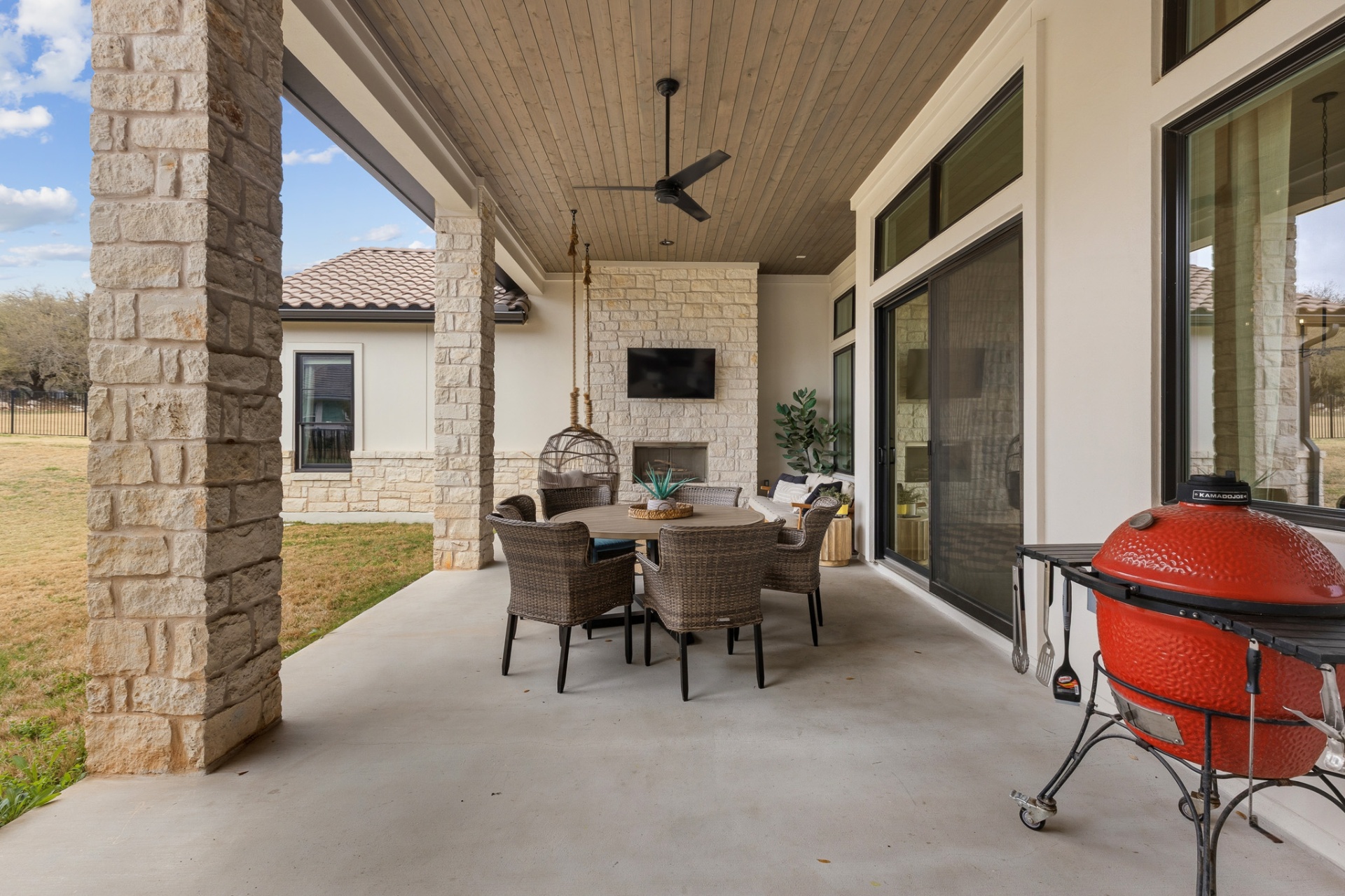 Covered patio — wicker dining set, Kamado Joe grill, stone fireplace, tongue-and-groove ceiling