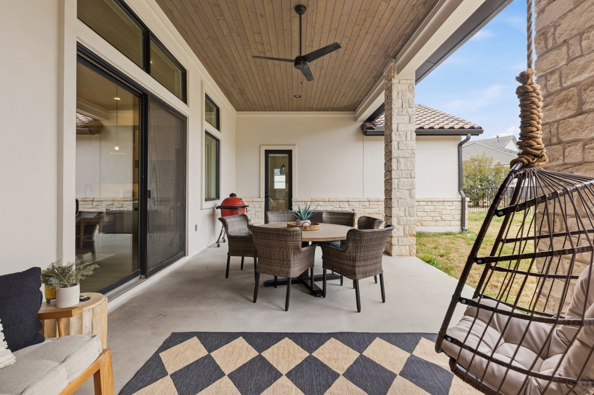 Covered patio — egg swing chair, diamond rug, wicker dining, Kamado Joe and backyard views