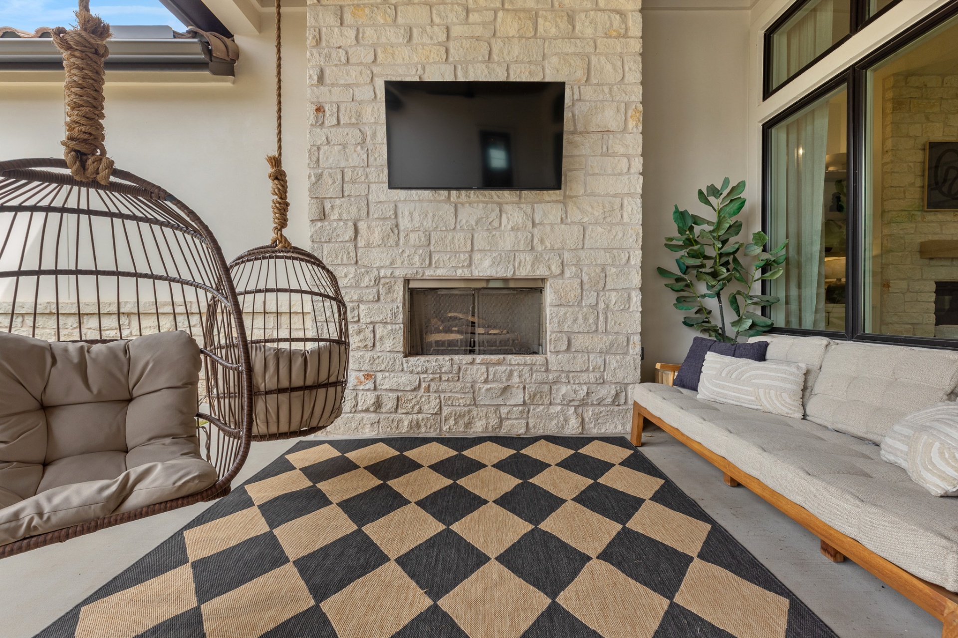 Covered patio outdoor living — limestone fireplace, wall-mounted TV, egg swings and outdoor sofa