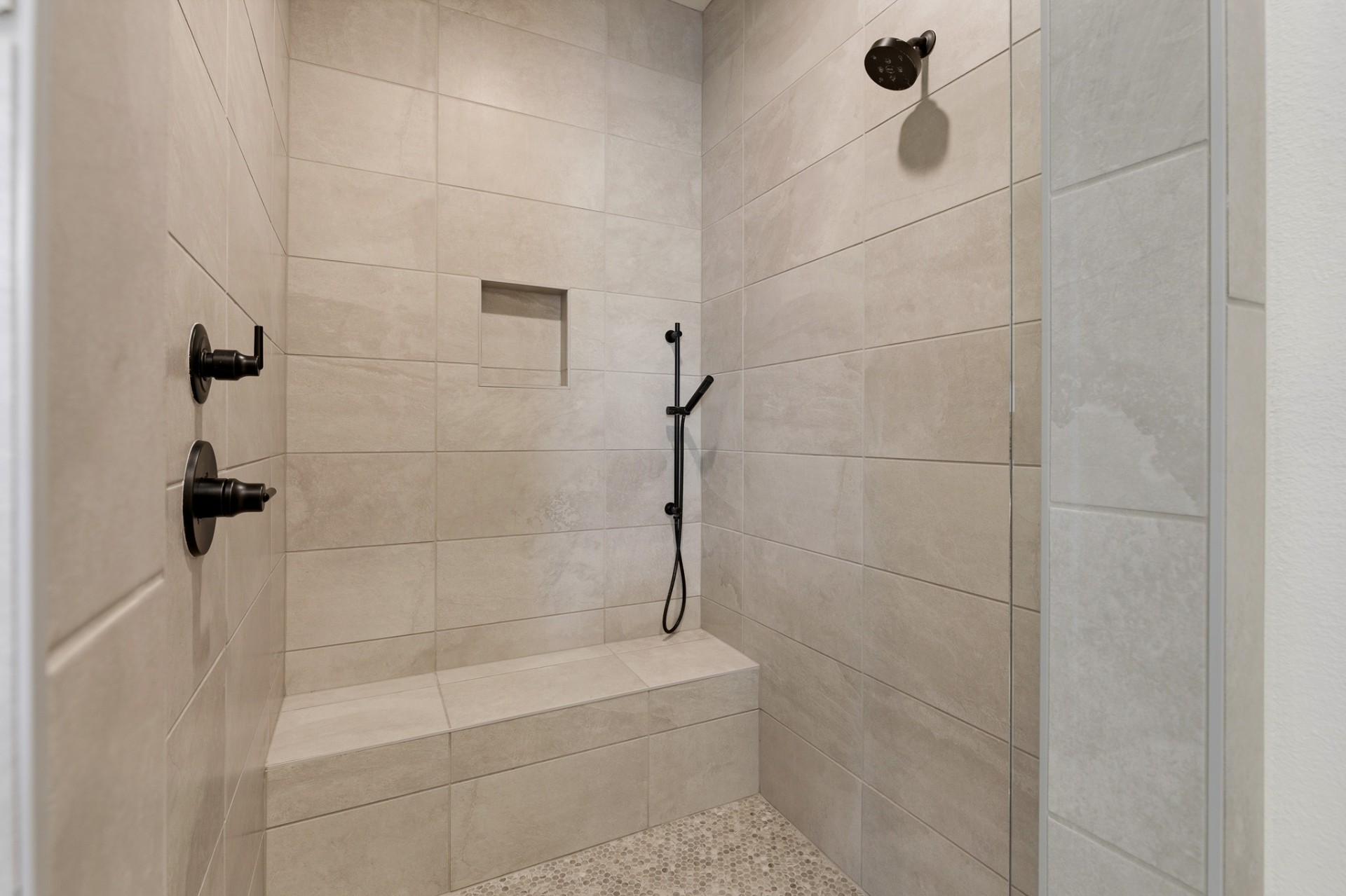 Primary bath walk-in shower with large-format tile, built-in bench, niche and black fixtures