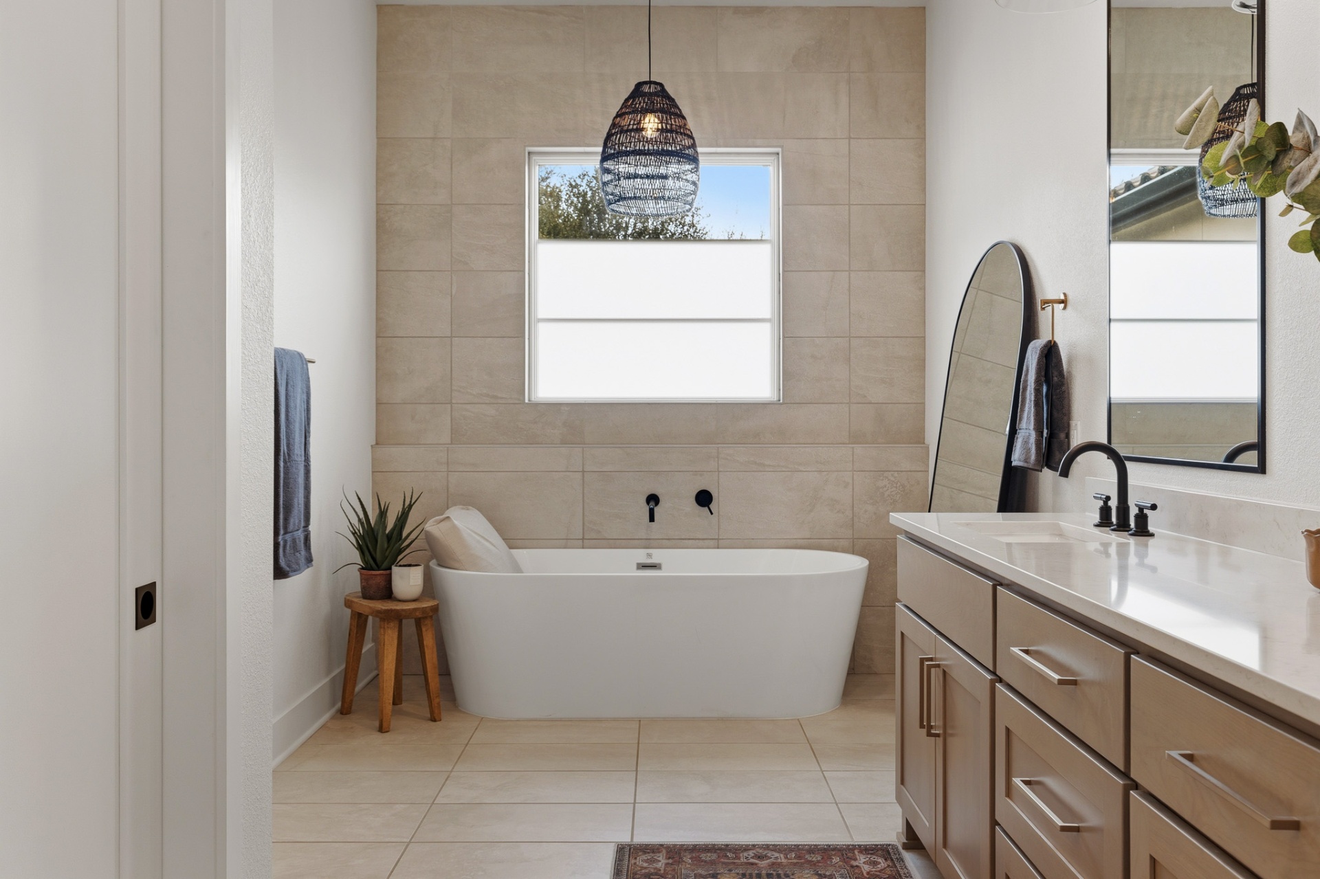 Primary bath freestanding soaking tub with woven pendant, stone tile wall and natural light