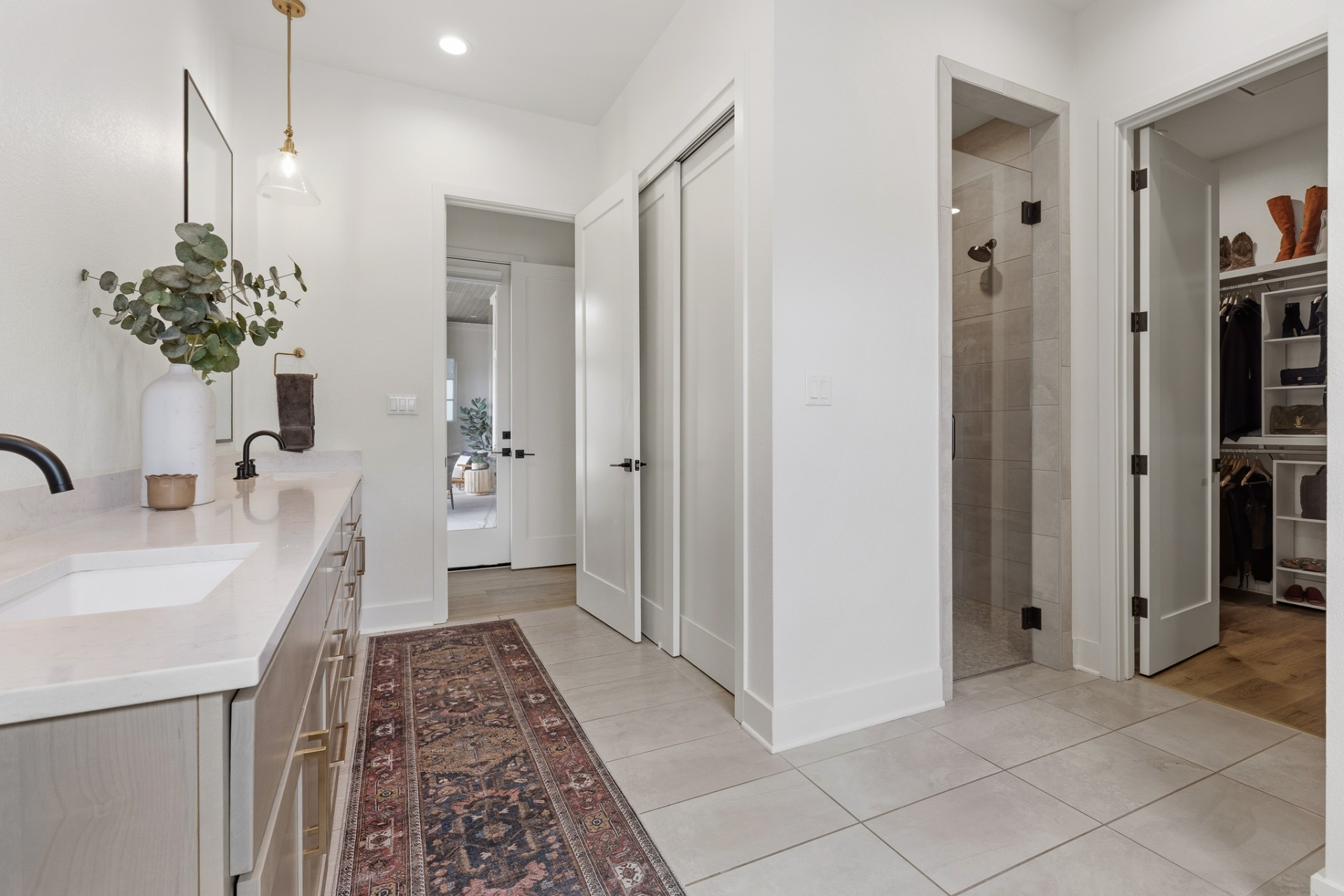 Primary bath vanity with quartz countertop, gold pendant, view to shower and closets