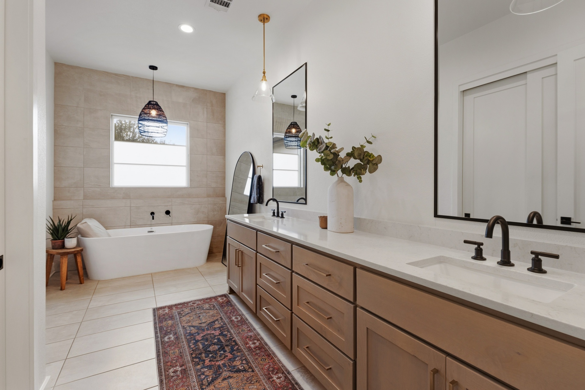 Primary bath — dual vanities with pendant lights, freestanding soaking tub and warm tile accent wall