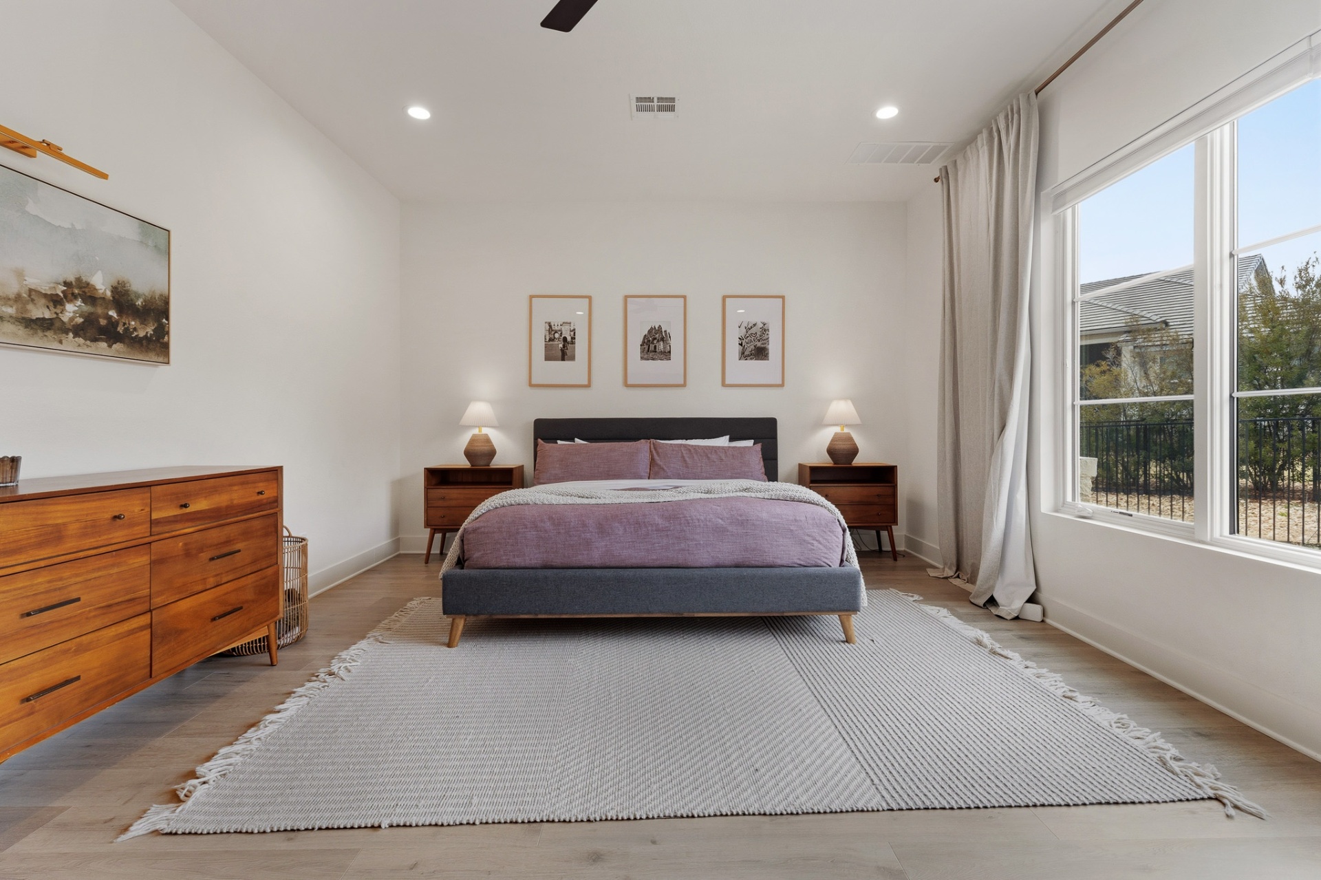 Primary bedroom angle with walnut dresser, framed art and backyard window view