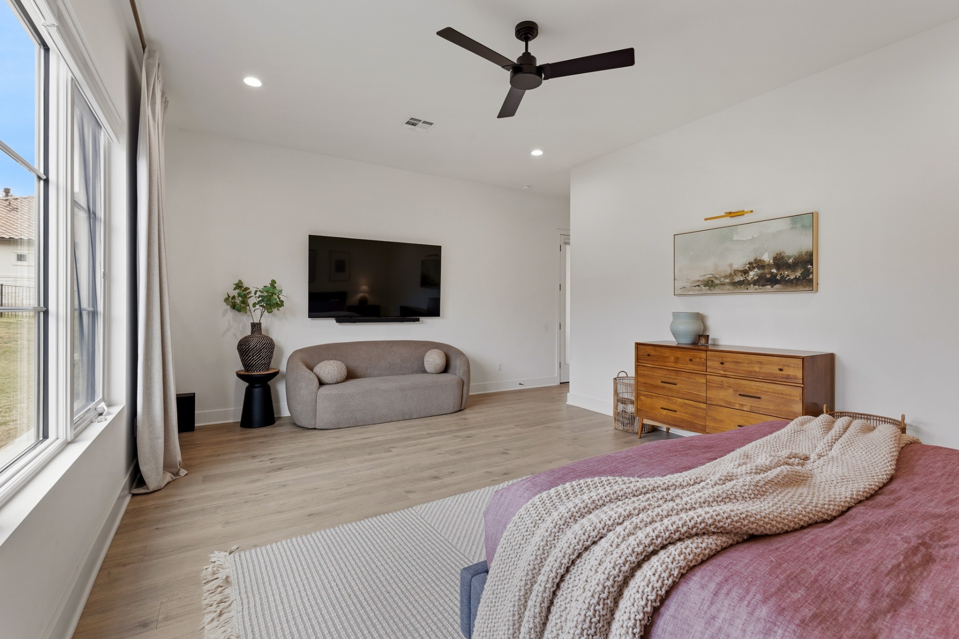 Primary bedroom sitting area with wall-mounted TV, curved sofa and black ceiling fan